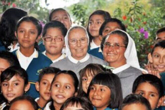 Dos hermanas marcelinas rodeadas de niñas y niños con uniforme escolar en el colegio El Girasol.